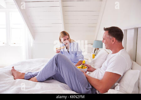 Paar Tragen Schlafanzug im Bett sitzen Essen Frühstück zusammen Stockfoto