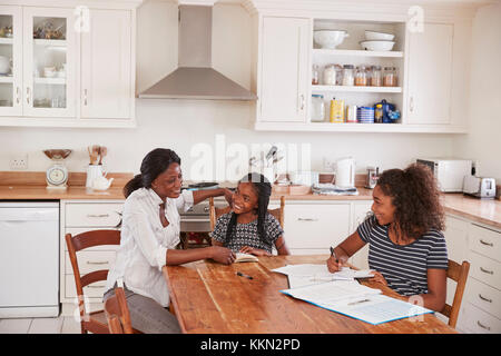 Mutter, zwei Töchter Sitzen am Tisch mit Hausaufgaben Stockfoto