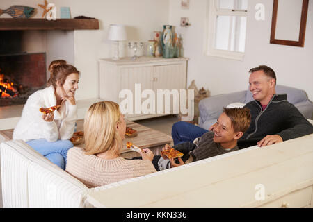 Familie sitzt auf einem Sofa in der Lounge am offenen Feuer essen Pizza Stockfoto