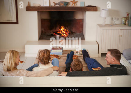 Familie sitzt auf einem Sofa in der Lounge am offenen Feuer Stockfoto