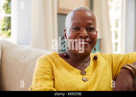 Portrait Of Smiling Senior Woman Sitting On Sofa zu Hause Stockfoto