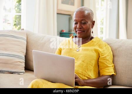 Ältere Frau sitzt auf einem Sofa mit Laptop zu Hause zusammen Stockfoto