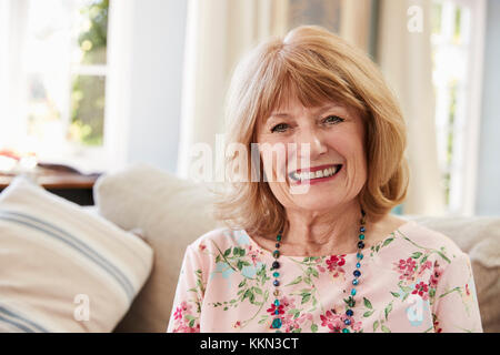 Portrait Of Smiling Senior Woman Sitting On Sofa zu Hause Stockfoto