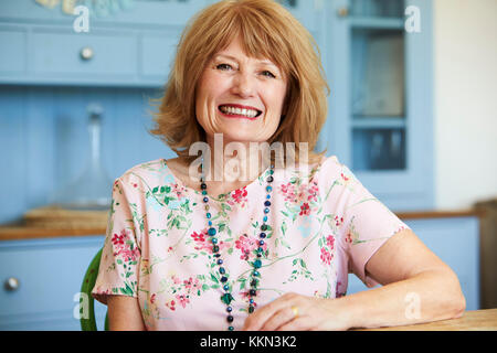 Portrait von lächelnden älteren Frau zu Hause sitzen am Tisch Stockfoto