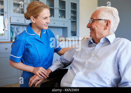 Krankenschwester im Gespräch mit älteren Mann sitzt im Sessel zu Hause besuchen Stockfoto