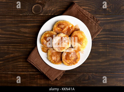 Krapfen, Quark Pfannkuchen mit karamellisierten Apfelscheiben auf hölzernen Tisch. top Aussicht, flach Stockfoto