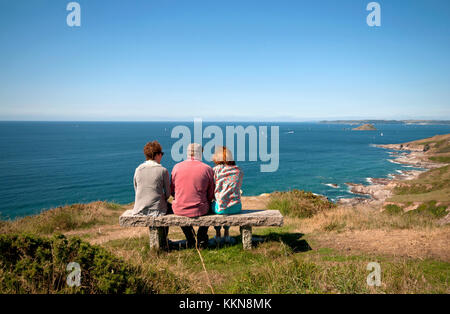 Drei Erwachsene sitzen auf einer Bank und bewundern die Aussicht auf die Südküste von Devon Stockfoto