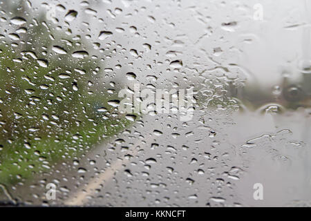 Mit Blick auf Strasse durch Auto Windschutzscheibe mit Regentropfen, das Fahren bei Regen. Stockfoto
