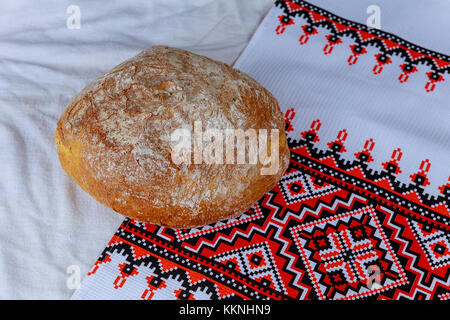 Hausgemachtes Brot und Salz auf dem Hintergrund der bestickte Handtuch. Vorderansicht. Es ist ein Ort für eine Inschrift. Das Konzept der Home Brot. Stockfoto