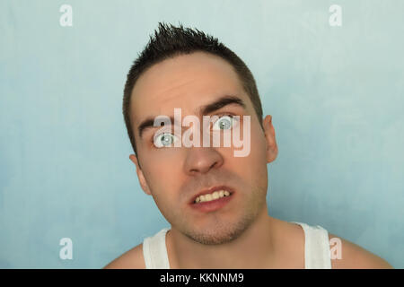 Porträt eines jungen Mannes mit Angst Ausdruck auf einem blauen Hintergrund. überrascht die Augen. Überrascht Emotion auf menschliches Gesicht. blue-eyed hübscher Kerl. Stockfoto
