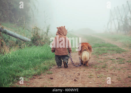 Kleinkind ist Laufen mit Hund im Nebel Stockfoto