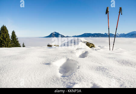 Paar Wanderstöcke und Fußspuren im Schnee. sportliche Aktivität in den Bergen Winter Landschaft. Allgäu, Bayern, Deutschland. Stockfoto