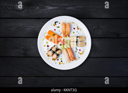 Sashimi auf eine weiße, runde Platte, mit kleinen Blumen, japanisches Essen, Ansicht von oben eingerichtet. schwarz Holz- Hintergrund Stockfoto