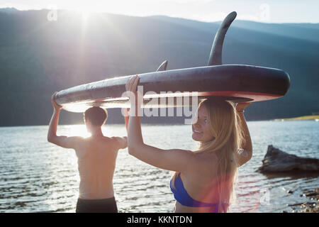 Paar Durchführung Stand up Paddle Board und zu Fuß in Richtung des Flusses Stockfoto