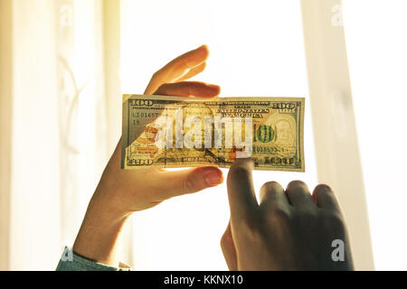 Kontrolle Falschgeld Licht. 100 Dollar gegen das Fenster in seiner Hand. Prüfen Sie auf Wasserzeichen auf Neue hundert Dollar Bill. Durchsichtigkeit des Amer Stockfoto