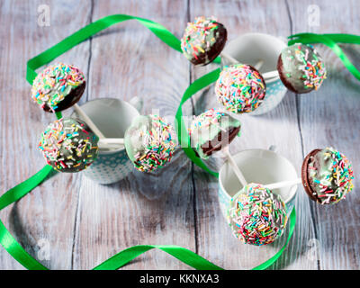 Nahaufnahme des bunten Schokoladenkuchen Pops mit Zucker Streusel in kleinen Tassen auf Holztisch. Kinder party Stockfoto