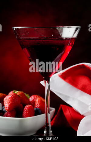 Foto von Kelch mit Cocktail mit Beeren auf rot beleuchteten backgroud Stockfoto