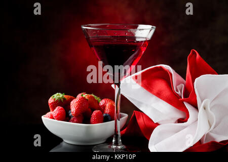 Foto von Kelch mit Cocktail mit Beeren auf rot beleuchteten backgroud Stockfoto