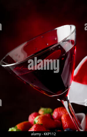 Foto von Kelch mit Cocktail mit Beeren auf rot beleuchteten backgroud Stockfoto