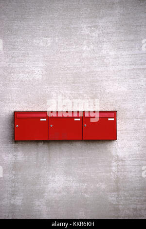 Drei rote Briefkästen in einer Reihe auf der rauen Betonfassade eines Gebäudes. Stockfoto
