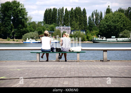 Zwei junge unbekannte Frauen sitzen auf einer Bank am Rhein in Mainz. Stockfoto