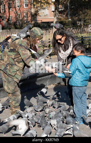 Larry, der Taube Männer in Washington Square Park, unterhält ein Kind und seine Mutter, wie sie die Tauben füttern und eine Masse der Vögel versammeln. Stockfoto