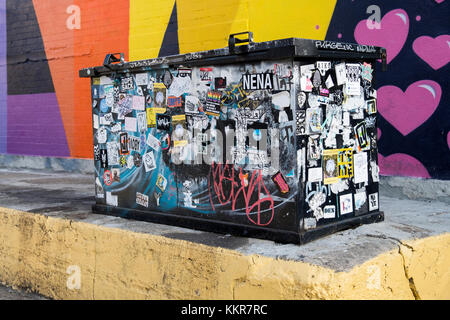 Ein Auffanggefäß holding Mülltonnen mit Graffiti, Flyer und Aufkleber im Abschnitt Bushwick in Brooklyn, New York. Stockfoto