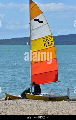 Segelyacht mit bunten Segel für den Start von zwei Jungen auf Sandstrand vorbereitet. Stockfoto