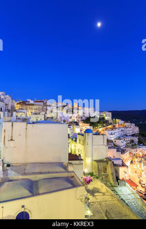 In der Altstadt von Peschici leuchtet das Licht, während der Dämmerung der Mond am Himmel ist. Apulien (Apulien), Italien. Stockfoto