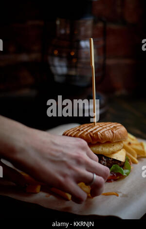 Der Mann nimmt die Burger. Der Chefkoch passt die Zutaten. Das Konzept des Fast Food Stockfoto