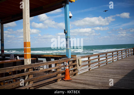 Holzsteg oder Promenade entlang auf Open air Restaurant auf einer Terrasse auf einem Florida Beach mit Blick auf einer ruhigen Ozean mit dem Brechen der Wellen auf einem sonnigen blauen Stockfoto