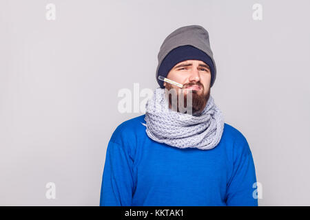 Junge Erwachsene bärtiger Mann haben, Temperatur, Thermometer im Mund. studio Shot, auf grauem Hintergrund Stockfoto