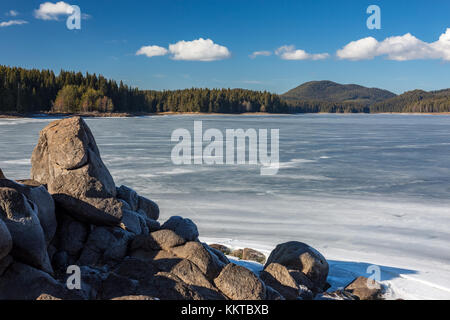 Schöne Felsformation, gefrorenen See Wasser, weißen Schnee auf dem Eis, weiße Wolken. Bulgarien, Rhodopen Gebirge, Shiroka Polyana See in einem sonnigen Winter Stockfoto