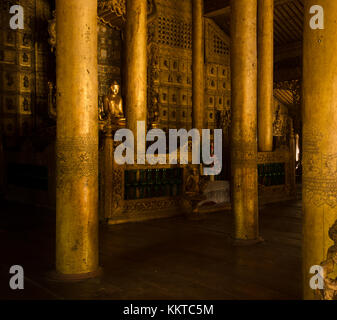 Eine vergoldete Statue des Buddha befindet sich auf dem Hauptaltar, unter einem Wald aus lackiertem Teakholz Spalten, in Kloster. schwenandaw Mandalay, Myanmar. Stockfoto