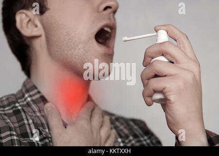 Ein junger Kerl spritzt in Kehle Remedy von weissen Spraydosen. Mann mit mundspray Close-up. erfrischende Atem Stockfoto