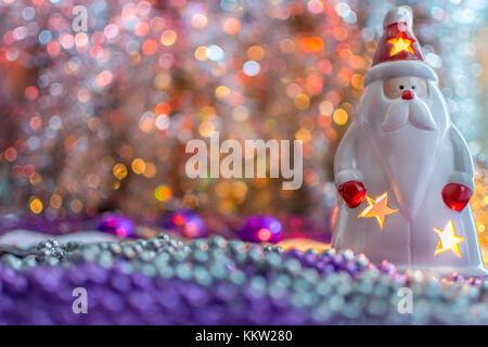 Bunte Weihnachtsdekorationen Santa mit einer Kerze im Innern, auf extrem geringe Tiefenschärfe und creamyorange Hintergrund. Stockfoto