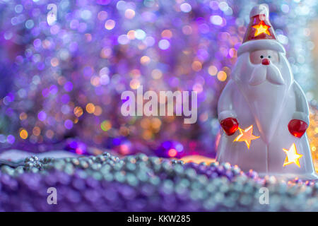 Bunte Weihnachtsdekorationen Santa mit einer Kerze im Innern, auf extrem geringe Tiefenschärfe und cremig violetten Hintergrund. Stockfoto