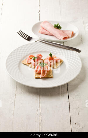 Foto von Cracker Vorspeise mit Schinken und Petersilie auf weißer Holztisch Stockfoto