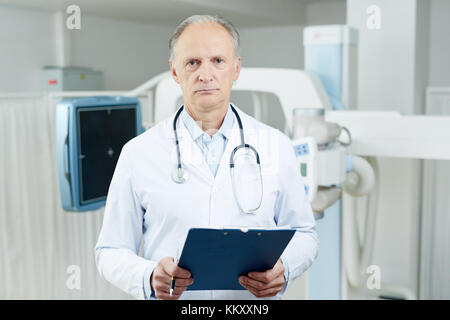 Ernsthafter erfahrener Arzt mit medizinischer Form, der während der Arbeit in die Kamera schaut Stockfoto
