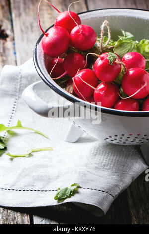 Frisches nass Radieschen in weiß Sieb über alten Holztisch Stockfoto