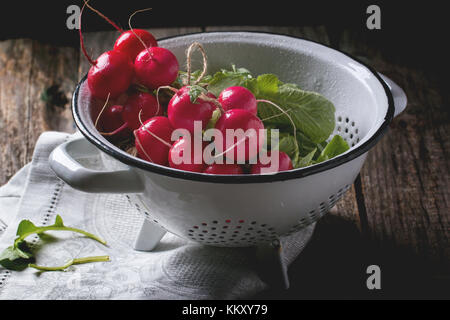 Frisches nass Radieschen in weiß Sieb über alten Holztisch Stockfoto