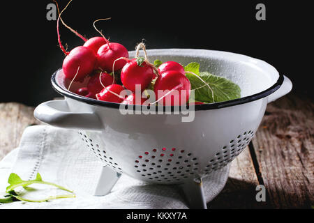 Frisches nass Radieschen in weiß Sieb über alten Holztisch Stockfoto