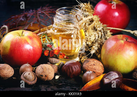 Glas Glas Honig mit Äpfeln, Ähren, Kastanien und Nüssen über schwarzen Holztisch Stockfoto