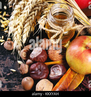 Glas Glas Honig mit Äpfeln, Ähren, Kastanien und Nüssen über schwarzen Holztisch. square Bild mit selektiven Fokus Stockfoto