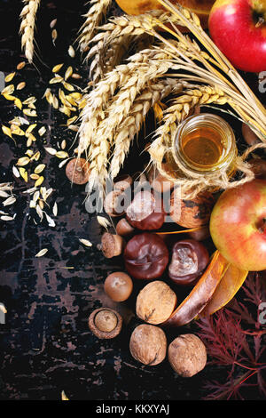 Glas Glas Honig mit Äpfeln, Ähren, Kastanien und Nüssen über schwarzen Holztisch. top View Stockfoto