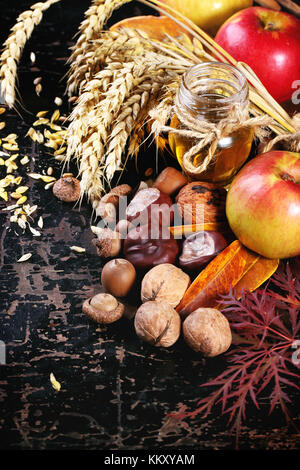 Glas Glas Honig mit Äpfeln, Ähren, Kastanien und Nüssen über schwarzen Holztisch Stockfoto