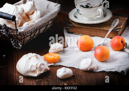 Hausgemachte Meringue, serviert mit Aprikosen und Vintage Tee Tassen über Holz- Tabelle. Stockfoto