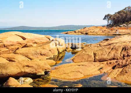 Blaues Wasser und Felsen farbige durch rote Flechten in den Freycinet National Park - Coles Bay, Tasmanien, Australien Stockfoto