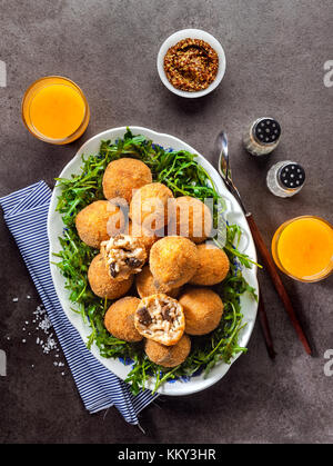 Italienische Snacks. Frittierte Kugeln aus Reis arancini mit Pilzen, Käse mit Senf Sauce und Salat mit Ruccola auf grauem Stein Tabelle mit frisch Squee Stockfoto