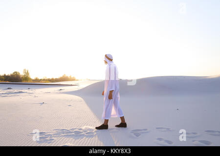 Stattliche junge muslimische entlang bodenlosen Wüste fahren und den Blick auf den Sonnenuntergang bewundern, die Schönheit der Natur auf warmen, klaren Nacht. Attraktive muslimischen smil